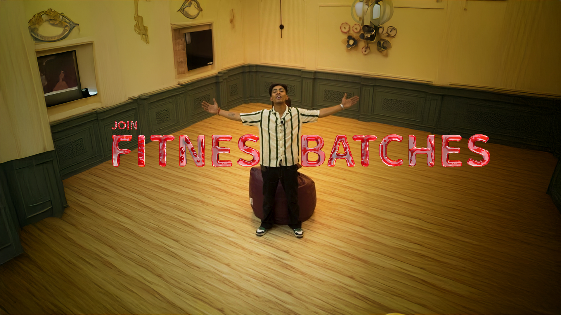 Man standing in the center of a wooden-floor studio with arms open wide, promoting fitness batches with bold red text overlay.