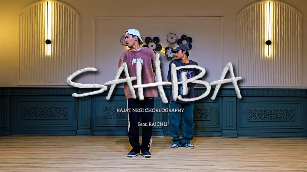 “Two male dancers performing choreography in a studio with elegant wall lights and wooden flooring, with ‘SAHIBAA’ title text overlay and Rajat Negi choreography credit.”